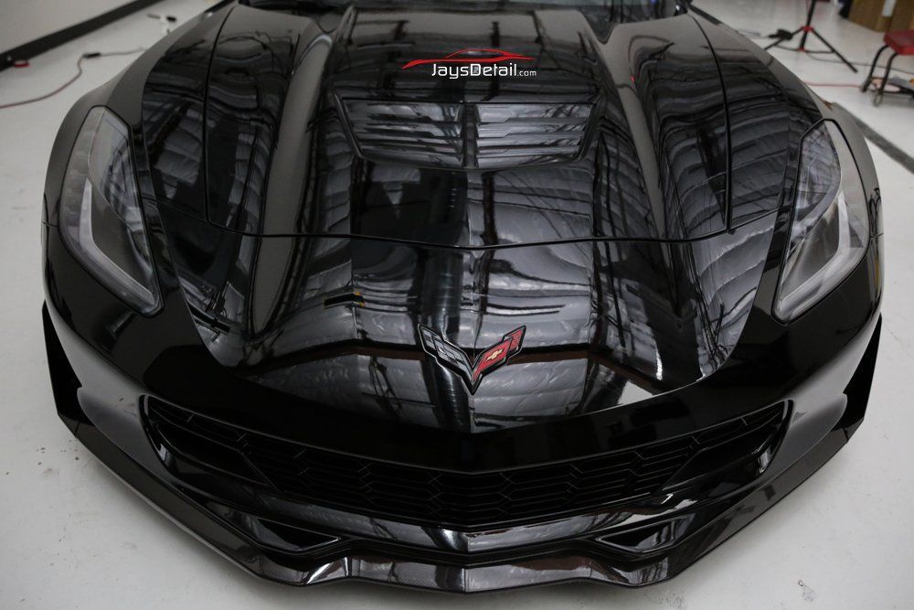 Black Corvette, hood reflecting room, with the Corvette emblem on the front.
