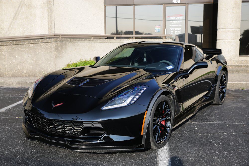 Black Chevrolet Corvette parked in front of a building with tinted windows; red brake calipers.