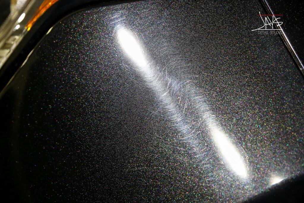 Close-up of dark car paint with visible swirl marks under bright lights.