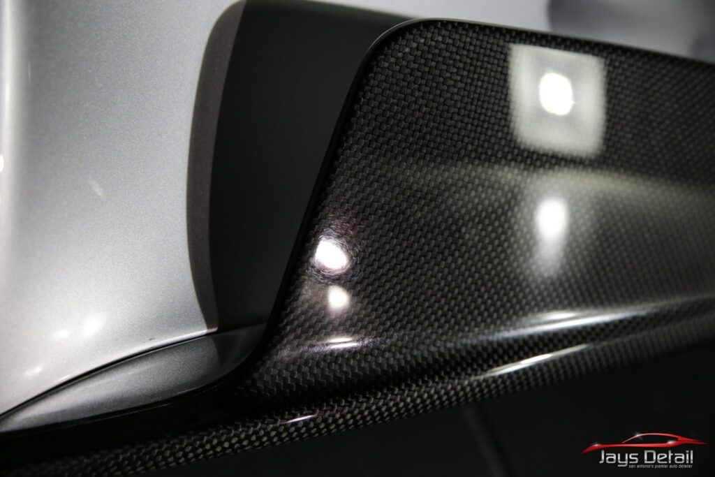 Close-up of glossy carbon fiber car spoiler, reflecting light. Black and gray tones.