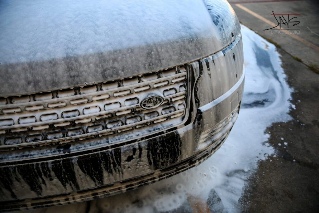Car's front end covered in white suds, parked on concrete, being washed.