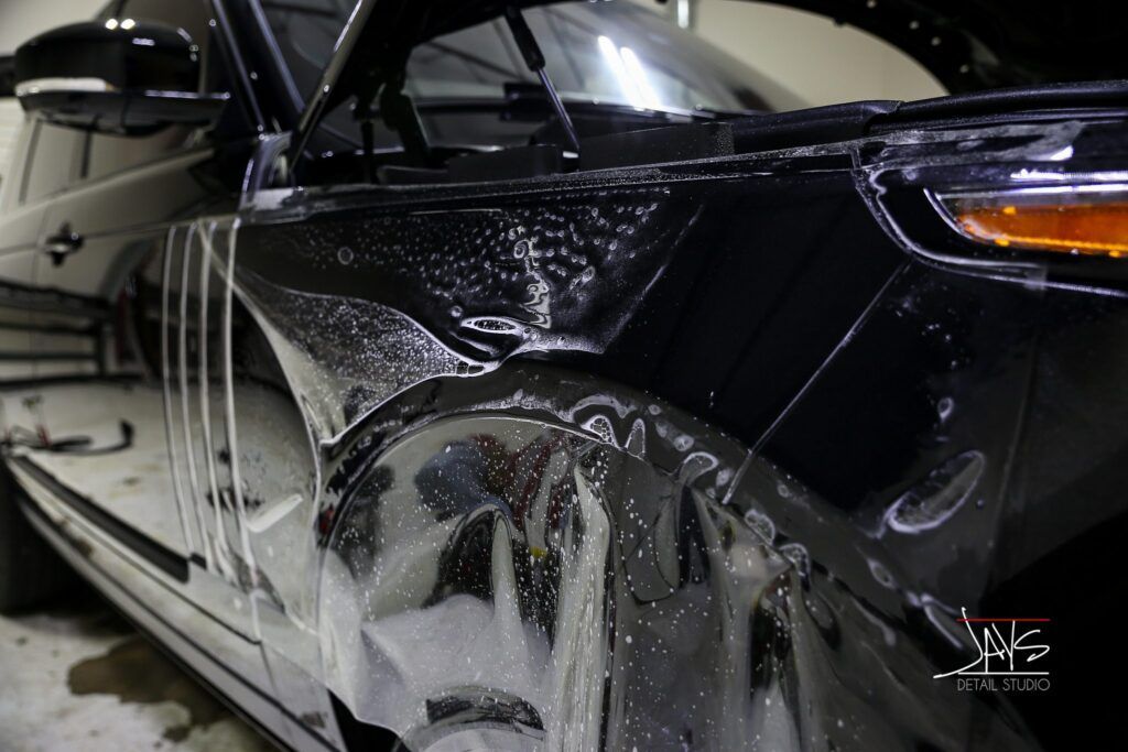 Black car being wrapped in protective film in a garage.