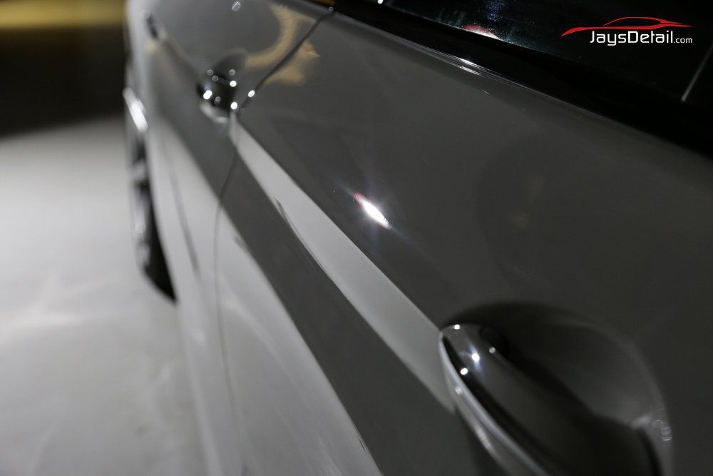 Close-up of a gray car door with a shiny, reflective surface. The handle is visible.