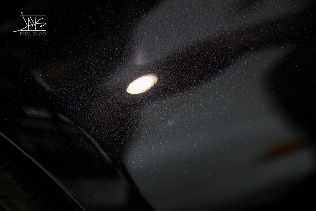 Black car hood with bright overhead light and water droplets.