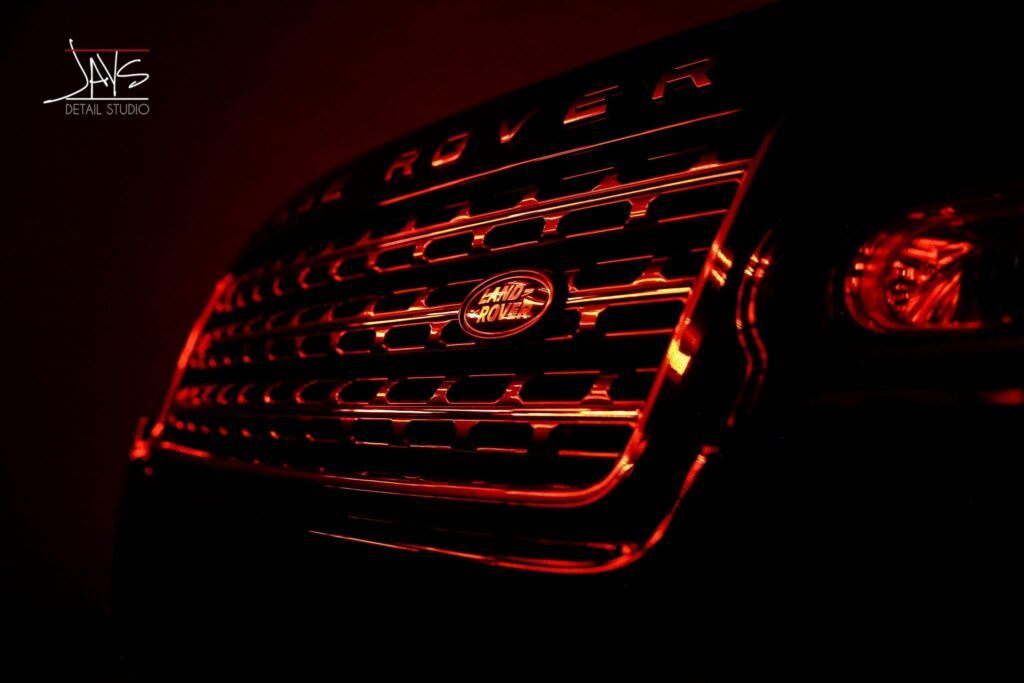 Close-up of a Land Rover grill, illuminated by red light. The Land Rover logo is centered.