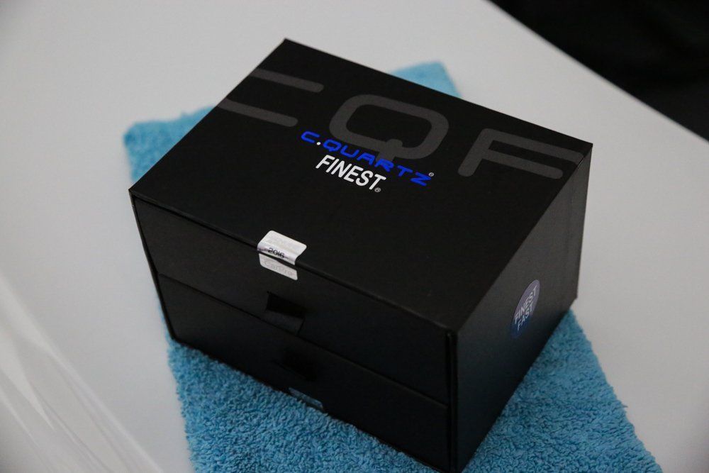 Black CQuartz Finest box on a blue towel, with white surface in the background.