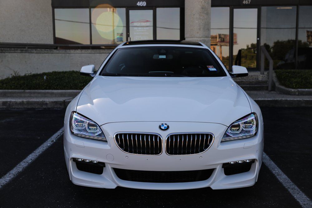 White BMW 6 series coupe parked in front of a building with glass doors; it is daytime.