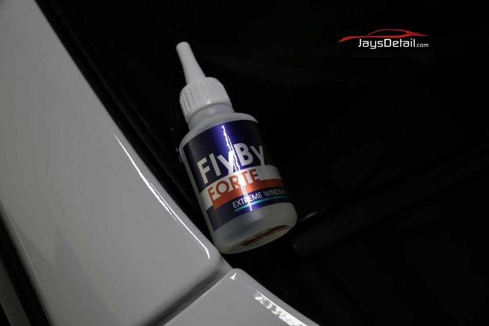 A bottle of Fixby Forte adhesive on a shiny white car surface.