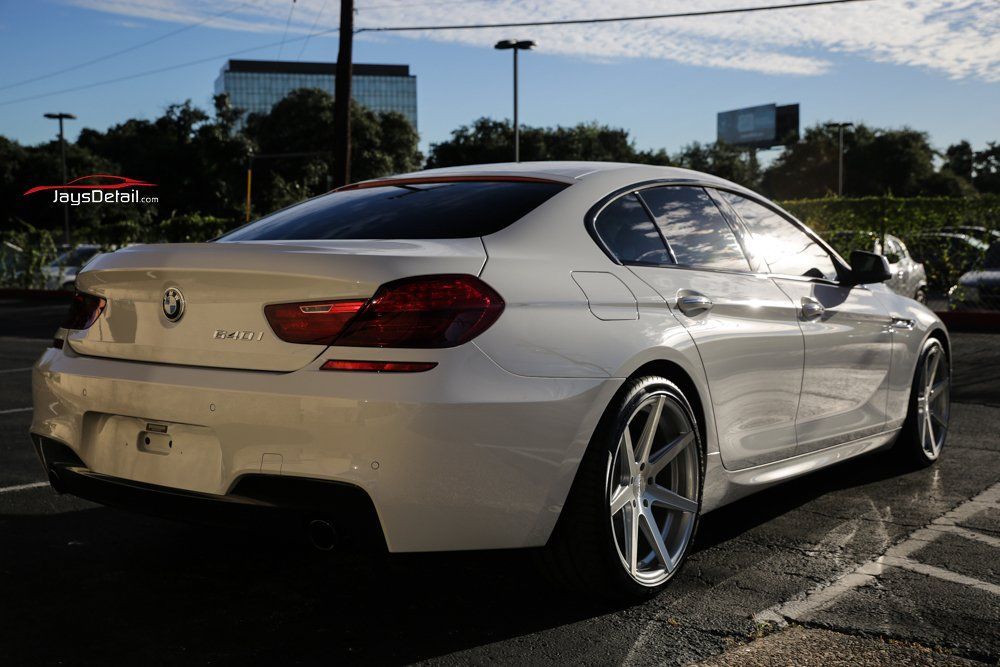 White BMW sedan parked in a lot with custom silver wheels. Daytime, outdoors.