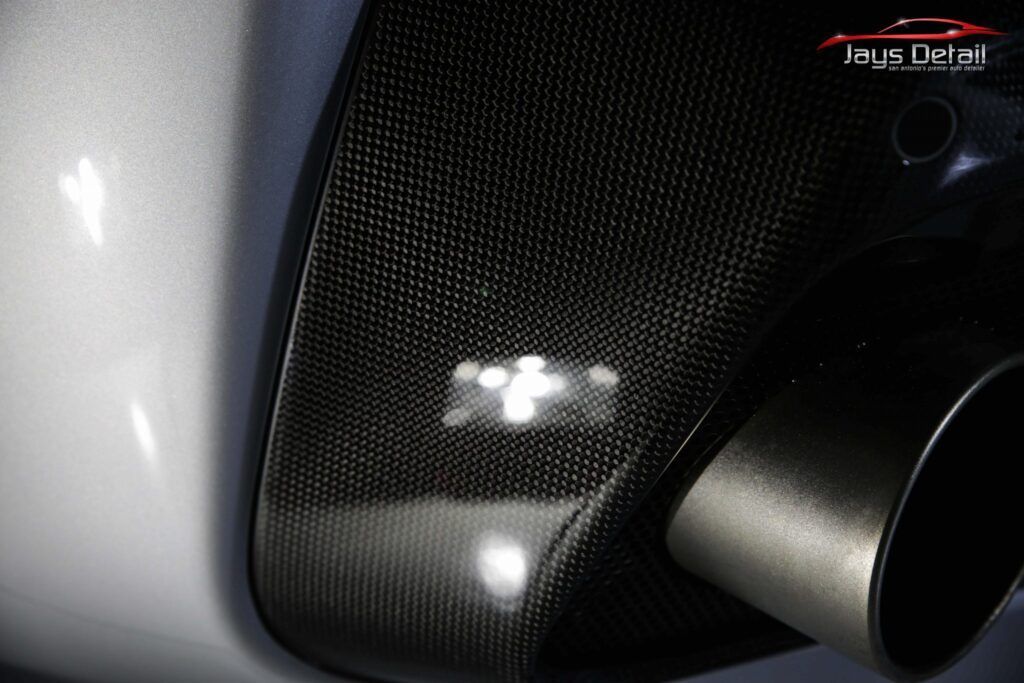 Carbon fiber car exhaust detail with silver tips and white body.