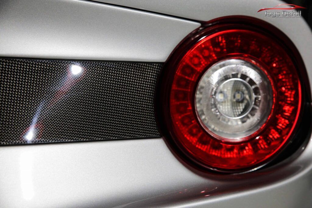 Silver car tail light with a red ring of lights, a clear center, and a carbon fiber strip.