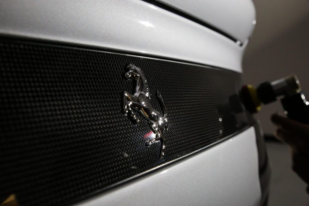 White Ferrari with carbon fiber trim, chrome emblem, being polished with a power tool.