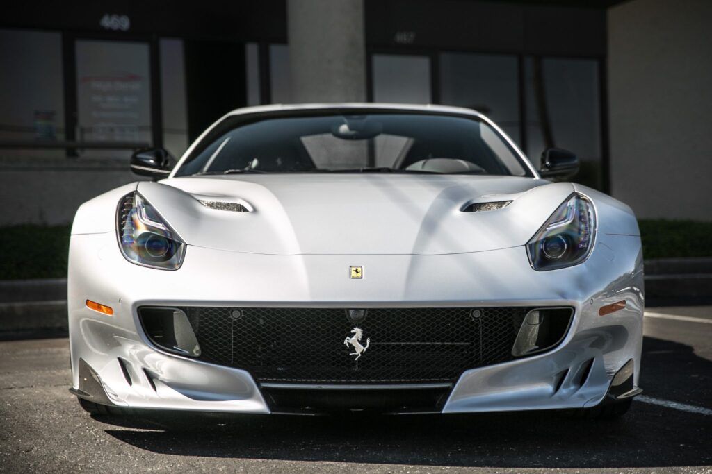 Silver Ferrari sports car parked in front of a building with black windows.