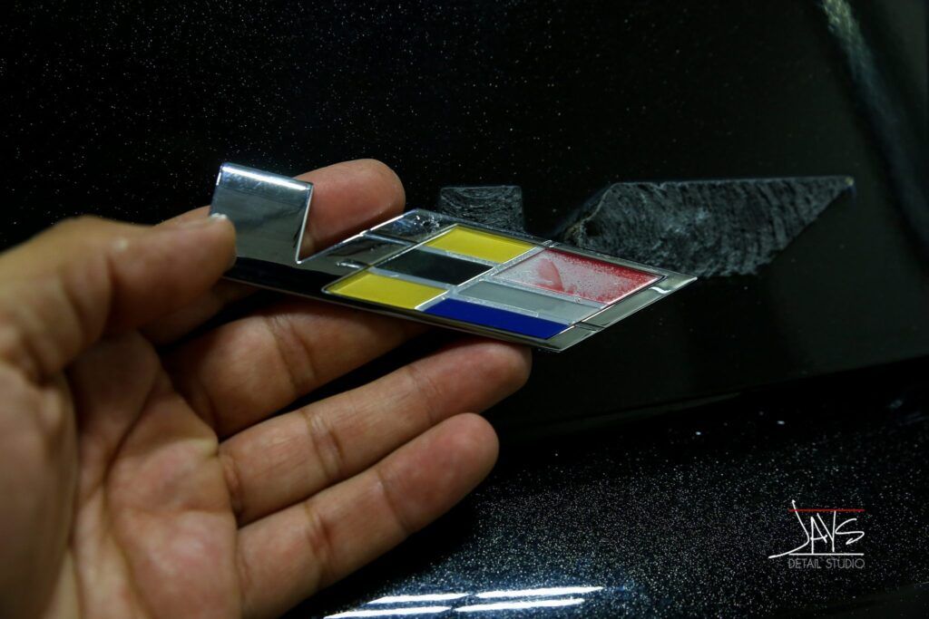 Hand holding a colorful car emblem with a black background.