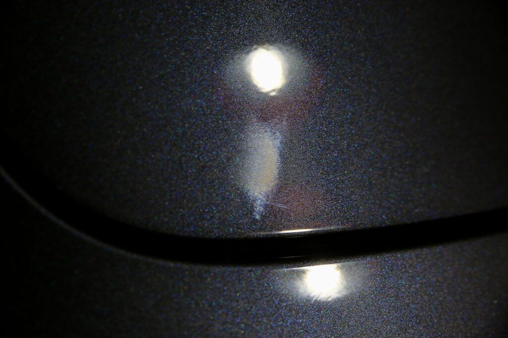 Close-up of a car's dark grey surface with a white spot and light reflections.