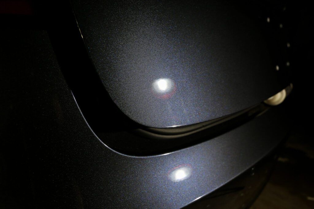Close-up of a dark gray, textured car surface, with light reflections.