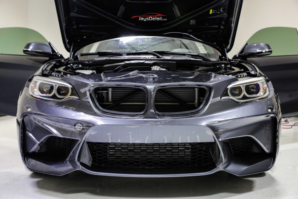 Dark gray BMW car with open hood, black grille, and open doors indoors.