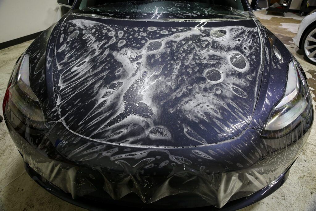 Tesla car hood covered in protective film with bubbles.