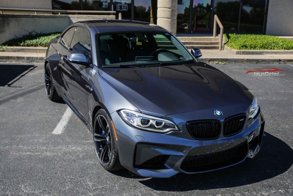 Gray BMW M2 coupe parked outside, showcasing its sporty design and black wheels.