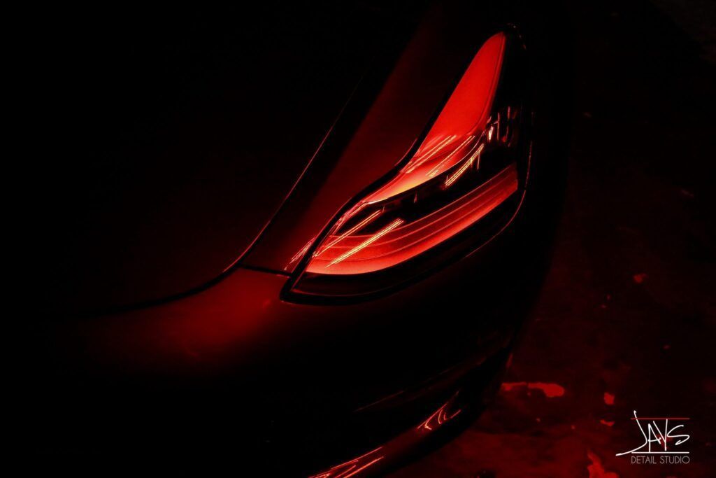 Red tail light of a dark car glows in the night.