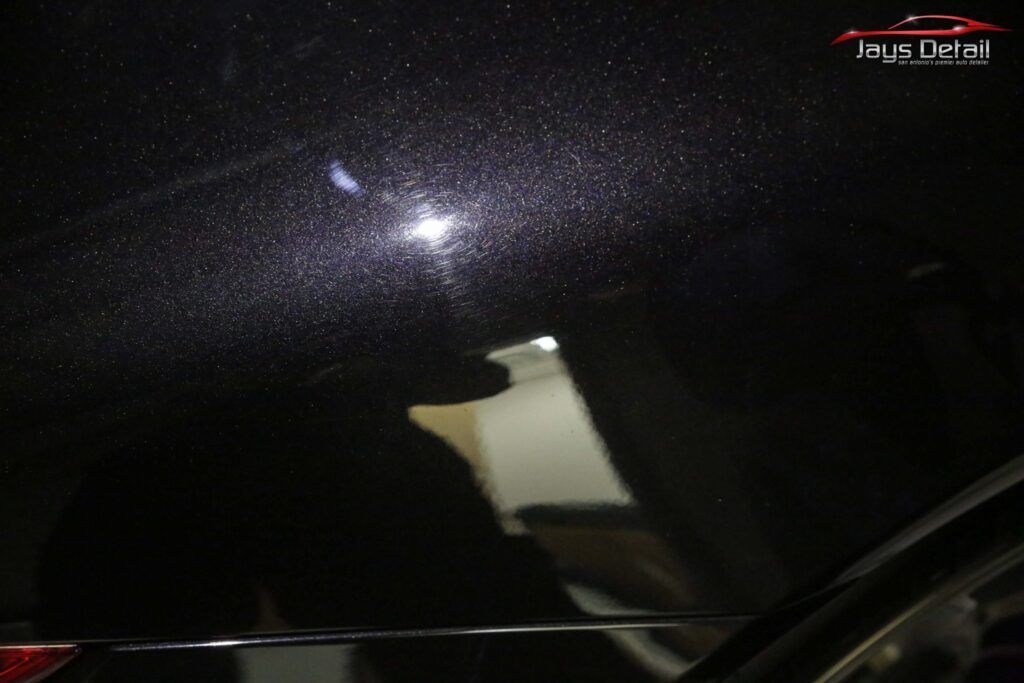 Black car roof with reflective speckles, light reflecting off it.