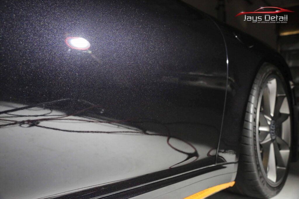 Close-up of a black car's shiny paint, showing reflections and a wheel.