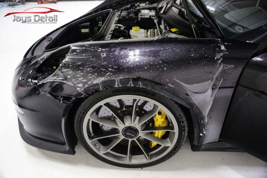 Car with clear protective film on its fender, revealing the vehicle's dark paint and yellow brake calipers.