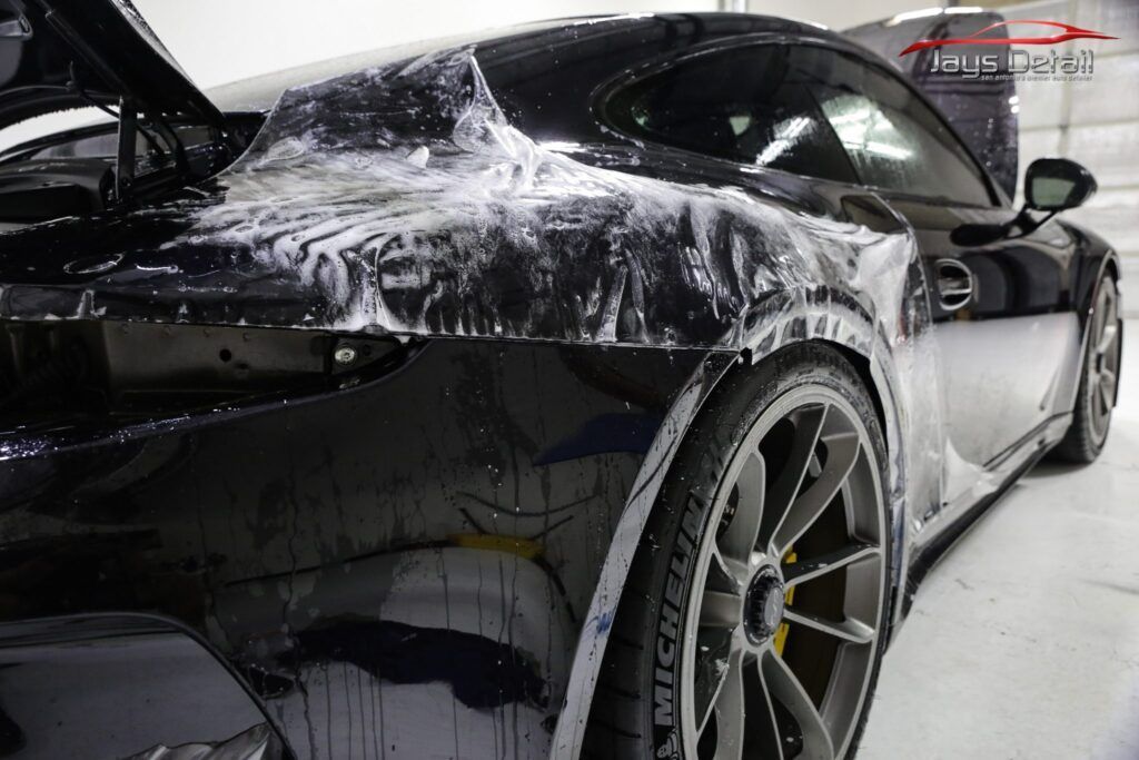 Black sports car with protective film being applied in a garage.