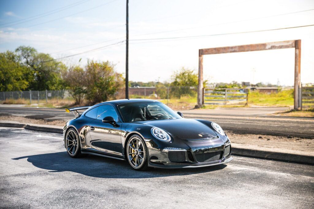 Black Porsche sports car parked on a paved road, daytime.