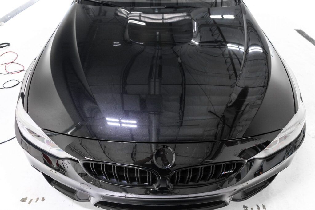 Black BMW car hood, shiny and reflective, in a brightly lit setting.