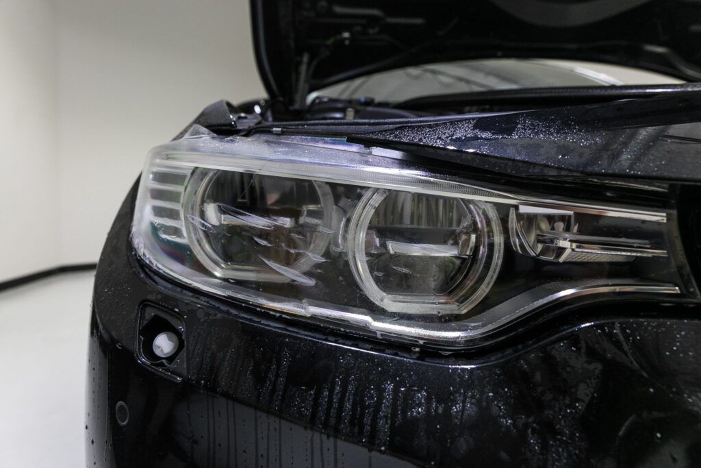 Black BMW car headlight with water droplets on the hood and an open hood.