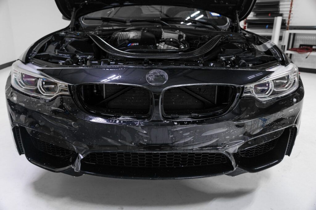 Black BMW car with the hood open, covered in soapy water, in a white room.