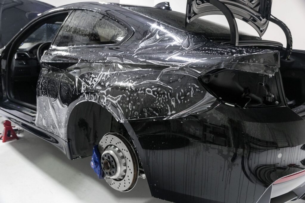 Black car with protective film being applied. Trunk and doors open.
