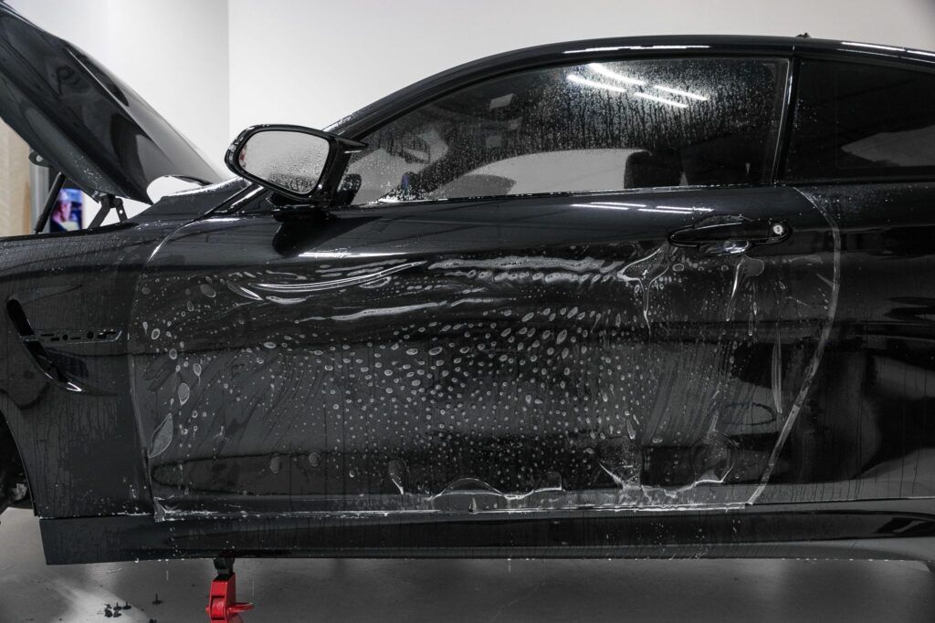 Black car being worked on, covered in soapy water.