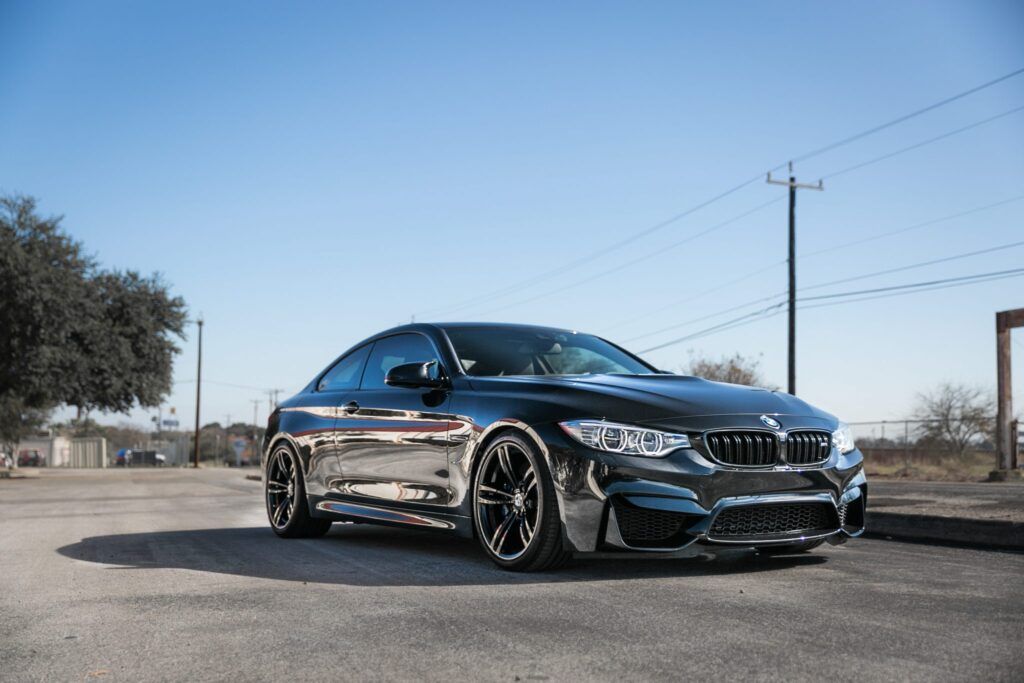 Black BMW M4 coupe parked on a road with a clear blue sky.