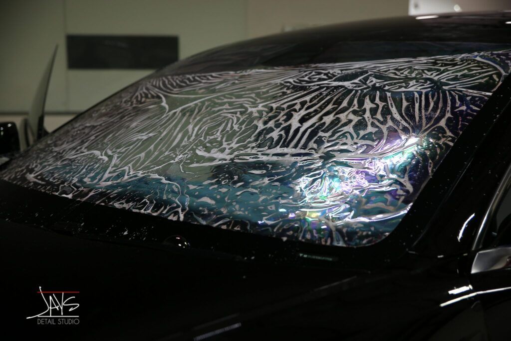 Windshield with wet film applied, showing a car in a workshop.