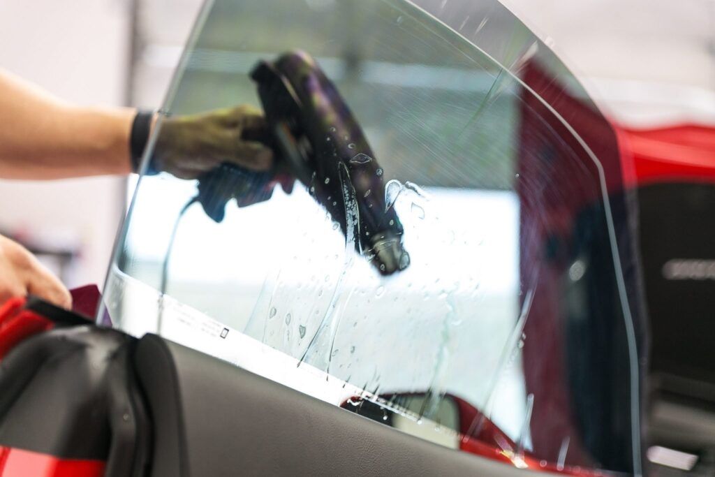 Person applying window tint to a car window with a heat gun, inside a garage.