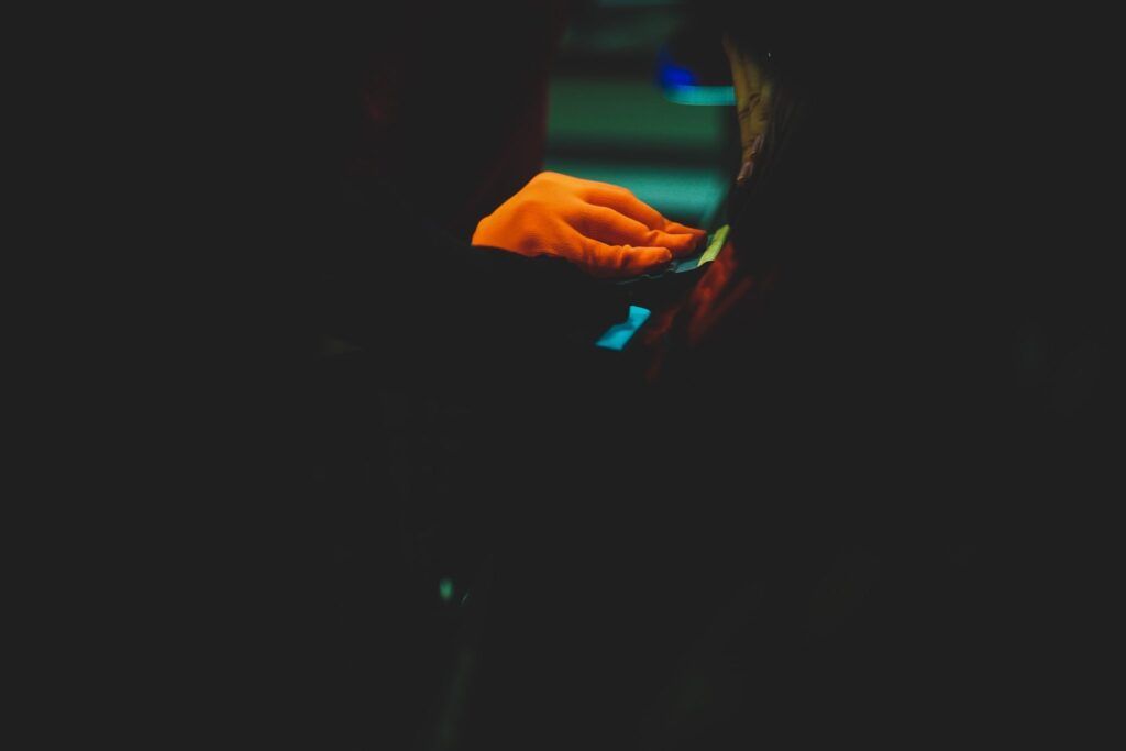 Person holding something orange in a dark setting, possibly a phone, with bright highlights.