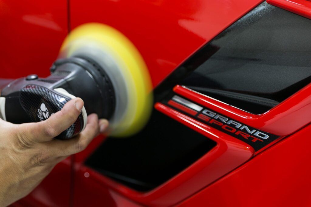 Person polishing a red car's vent with a buffing machine, close up.