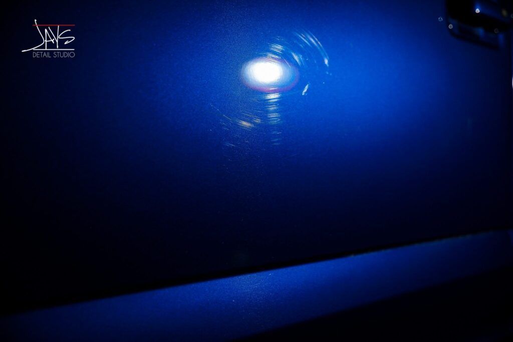 A bright light reflecting on a blue surface, showing swirls and imperfections.