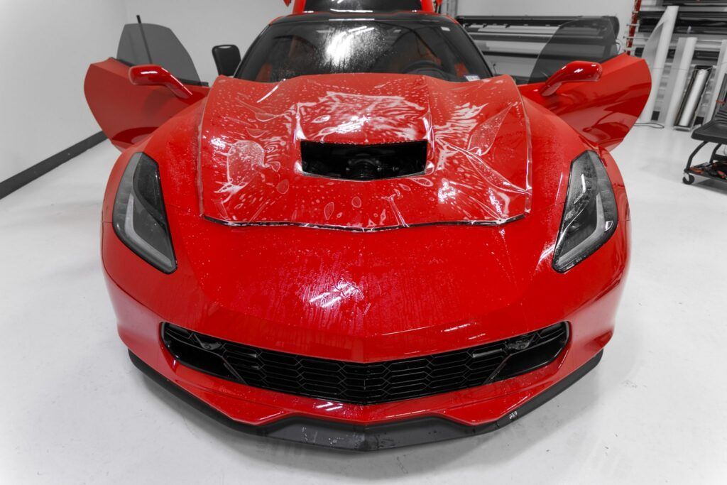 Red sports car with doors open, covered in protective film.