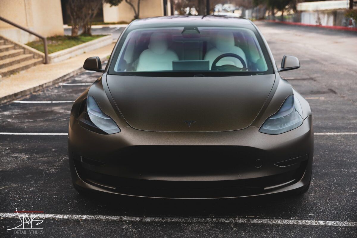 Brown Tesla car parked in an asphalt parking lot.