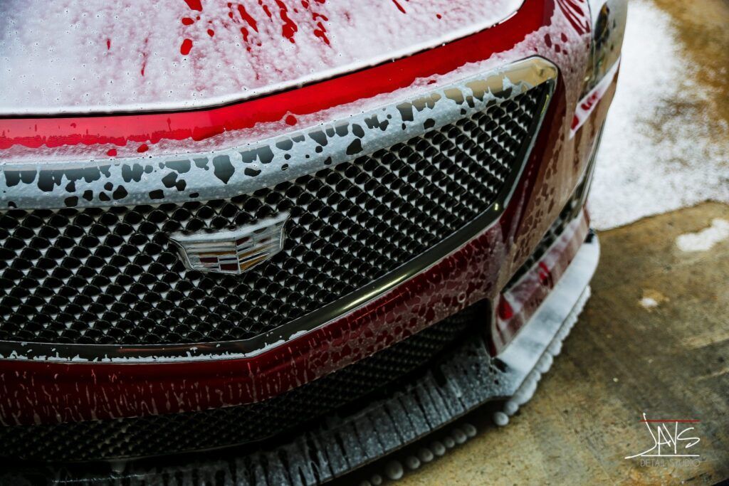 Red Cadillac grill covered in soapy foam.