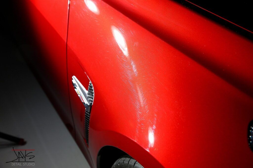 Red sports car fender with white water spot stains, shiny finish.