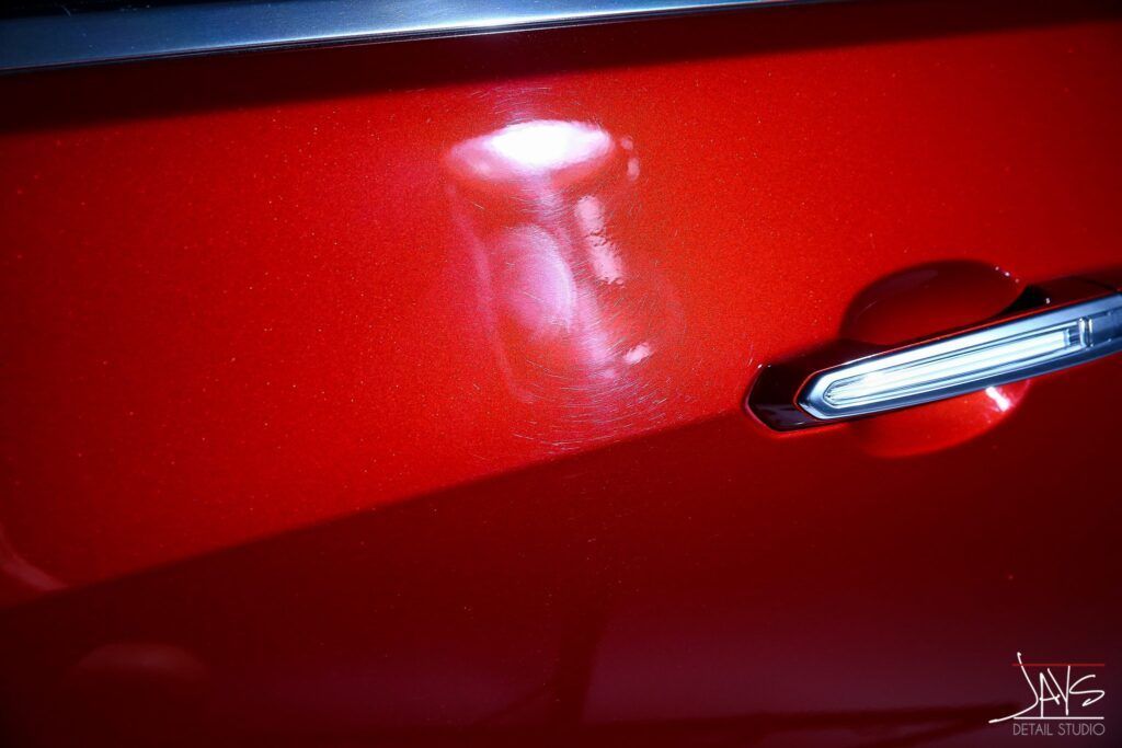 Red car door with a dent, near the handle.