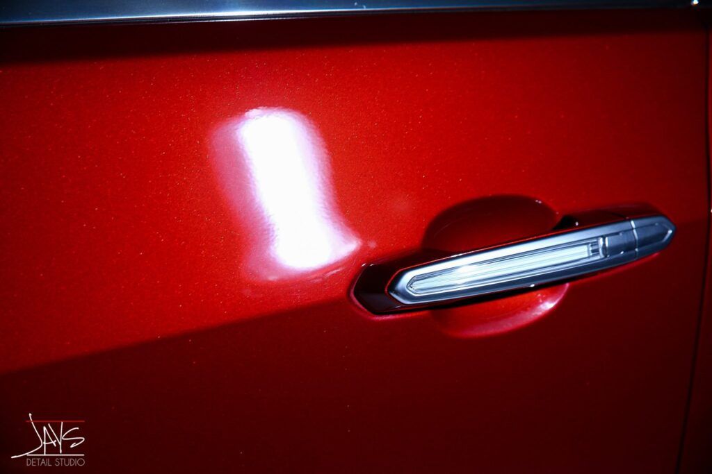 Red car door with a recessed handle and bright light reflection.