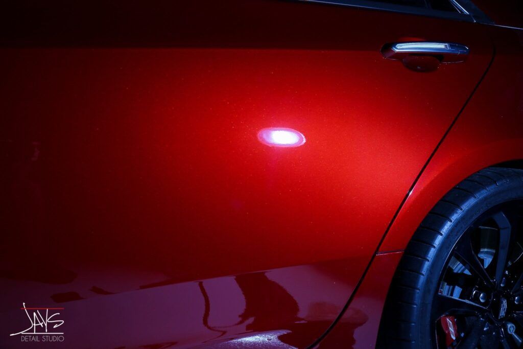 Red car door reflecting a light. Black wheel visible on the right.