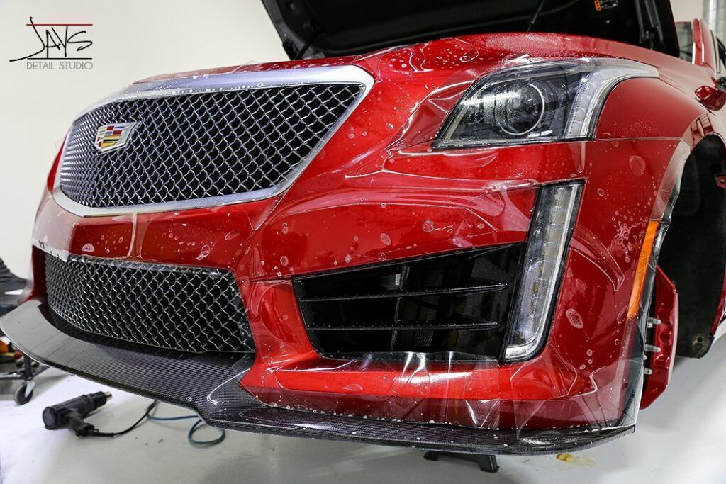 Red Cadillac front bumper with clear protective film being applied.