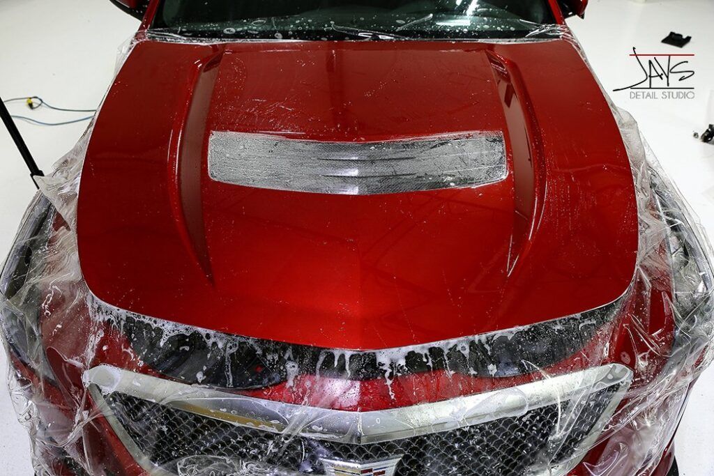 Red car hood covered in protective film, wet with solution.