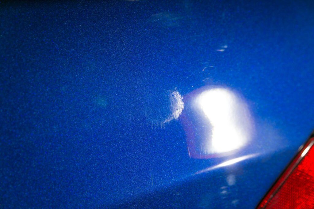 Blue car paint with a bright white scratch and a red taillight corner.